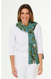Türkis-grüner Schal mit abstraktem Muster in Blau, Braun und Beige, lang, locker um den Hals gelegt, getragen von lächelnder Frau in weißem Langarmshirt und weißer Hose, frontal stehend