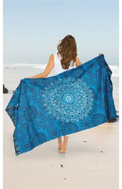 Blaues Strandtuch mit mandalaähnlichem, symmetrischem Muster in Hellblau und Weiß, rechteckig, gehalten von einer stehenden Frau mit langen braunen Haaren, weißem ärmellosem Oberteil, am Strand
