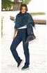Blau-grüner Schal mit geometrischem Muster und Fransen, um die Schultern einer stehenden Frau gelegt, kombiniert mit dunkelblauen Jeans und blauen Sneakers