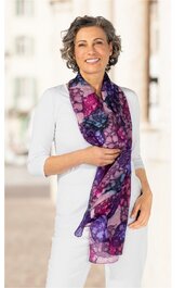 Langer Schal in Violett- und Pinktönen mit kreisförmigem Muster, transparentes Design, locker um den Hals getragen von lächelnder Frau mit weißem Oberteil und grauen kurzen lockigen Haaren, federleicht