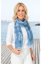 Hellblaue Rechteckschal mit weißem Paisleymuster, getragen von stehender Frau mit weißen 3/4-Arm-Shirt und weißen Hosen, Meer und Holzsteg im Hintergrund