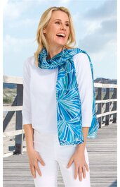 Blauer Schal mit türkis-weißen floralem Muster, lang, locker um den Hals getragen von stehender Frau in weißem Langarmshirt und weißer Hose, Outdoor auf Holzsteg mit Geländer und Himmel im Hintergrund