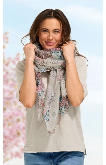 Hellbeiges Kurzarmshirt mit Rundhalsausschnitt, getragen von stehender Frau, dazu gemusterter Schal in Pastellfarben mit geometrischen Motiven, Schal locker um den Hals gelegt, blaue Jeans