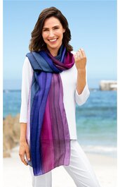 Schal in Blau-, Violett- und Pinktönen mit Farbverlauf, dünn, lang, getragen von lächelnder Frau mit weißer Bluse und weißer Hose am Strand, locker um den Hals gelegt