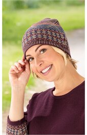 Strickmütze mit buntem, geometrischem Muster in Blau, Rot und Grau, eng anliegend, getragen von lächelnder Frau mit blondem Haar, hochgekrempelter Pullover in Dunkellila mit passendem Muster am Ärmel