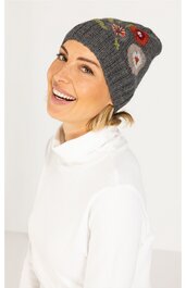 Grau melierte Strickmütze mit bunten Blumenstickereien, schmale Passform, getragen von lächelnder Frau mit weißem Rollkragenpullover, Mützedeckung bis über die Ohren