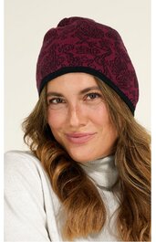 Dunkelrote Beanie-Mütze mit schwarzem Blumenmuster, schwarzer Umschlagkante, getragen von lächelnder Frau mit langen, welligen, hellbraunen Haaren, weißer Rollkragenpullover