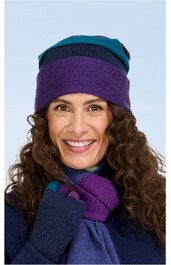 Damenmütze in Lila und Dunkelgrün, gestreift, mit Umschlag, getragen von lächelnder Frau mit offenen braunen Locken, dazu passende lila Handschuhe und Schal, gestrickt