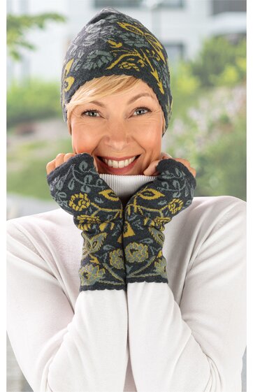 Gestrickte Mütze und Fingerlose Handschuhe in Anthrazit mit gelb und hellblau floralem Muster, Mütze spitz zulaufend, Handschuhe lang, getragen von lächelnder Person in weißem Oberteil, eng anliegend