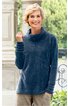 Dunkelblauer Pullover mit hohem Kragen, lange Ärmel mit gesteppten Riegeln, lockere Passform, getragen von lächelnder stehender Person vor Steinwand und Grünpflanzen