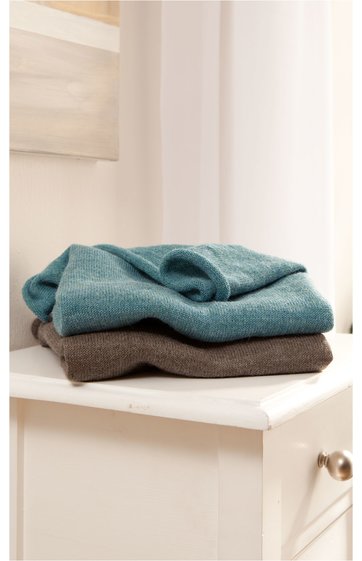 Zwei gefaltete Decken oder Wolldecken, obere Decke petrolblau, untere Decke dunkelbraun, glatt gewebt, liegen auf weißem Möbelstück