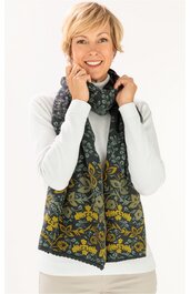 Dunkelgrüner Schal mit floralen gelben und grauen Mustern, lang, lose um den Hals einer lächelnden Frau mit kurzen blonden Haaren, getragen zu weißem Pullover und beiger Hose
