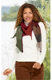 Weißer Pullover mit Rundhalsausschnitt, getragen von stehender Frau, braune Cordhose, mehrfarbiger Schal mit Streifenmustern in Rot-, Braun- und Grautönen, lange lockige Haare