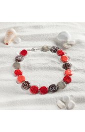 Halsschmuck aus flachen, rundlichen Perlen in Rot-, Braun- und Grautönen mit verschiedenen Mustern, Schmuck auf heller Sandoberfläche mit Muscheln angeordnet