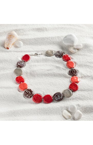 Halsschmuck aus flachen, rundlichen Perlen in Rot-, Braun- und Grautönen mit verschiedenen Mustern, Schmuck auf heller Sandoberfläche mit Muscheln angeordnet