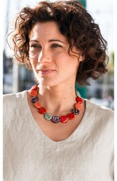 Collier aus großen Perlen in Rot, Violett und Weiß mit Spiralmuster, getragen von Frau mit lockigem braunem Haar, dazu weiße Bluse mit rundem Ausschnitt