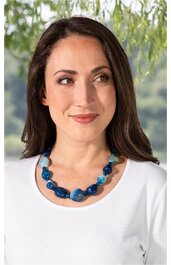 Blau und türkisfarbene Perlenkette mit runden und ovalen Elementen, getragen von Frau mit weißen Oberteil, sichtbare Schultern, keine weiteren Details
