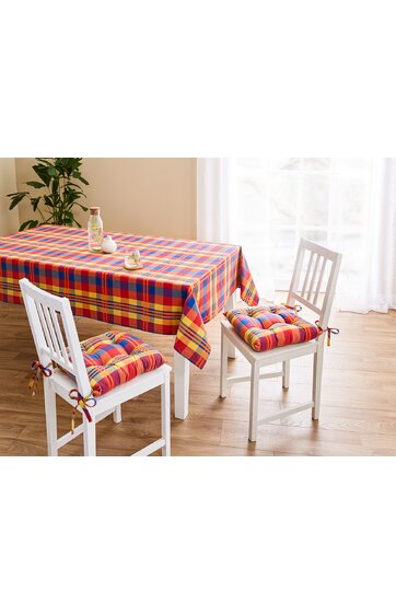 Rechteckige Tischdecke in rot, gelb, orange, blau kariert auf weißem Esszimmertisch, zwei weiße Stühle mit passenden karierten Sitzkissen, Holzfußboden, helle Vorhänge, Pflanze im Hintergrund