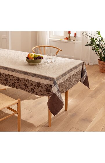 Rechteckige Tischdecke in beige und braun mit floralem Muster, breite gemusterte Bordüre, auf Esstisch mit Holzbeinen, einzelne Glasgläser und Schale mit Obst darauf, helle, minimalistisch eingerichtete Küche