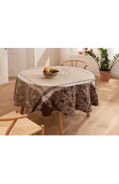 Runder Esstisch mit braunem Tischbezug mit dunklem Blumenmuster, darüber liegender beiger Tischdecke mit lichtgrauem Blumenrand, Holzstühle mit geflochtener Sitzfläche, auf Tisch Schale mit Obst und zwei Gläser, heller Holzboden, Pflanze im Tonkrug,