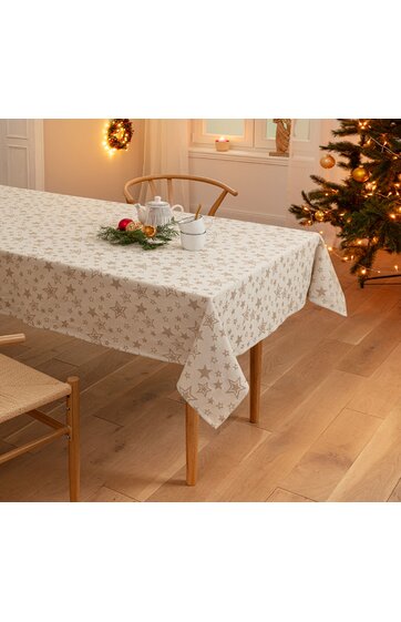 Tischdecke in cremeweiß mit silbernen Sternen und Schneeflockenmuster, rechteckig, auf Holztisch, gedeckt mit weißem Tee-Set und Weihnachtskranz, helles Esszimmer mit Holzstuhl und dekoriertem Weihnachtsbaum im Hintergrund