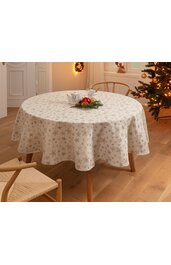Runder Tisch mit cremefarbenem Tischdecke mit goldfarbenem Sternenmuster, leicht überhängend, darauf weiße Kaffeekanne und Tasse auf Untertasse, Tisch steht in hellem Raum mit Holzboden, im Hintergrund Weihnachtsbaum mit Lichterkette und Stuhl
