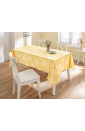Gelbe rechteckige Tischdecke mit weißen Blumenmustern, liegt auf weißem Tisch, umgeben von weißen Stühlen, im hellen Raum mit Holzboden, Blumenvasen auf Tisch und Fensterbank