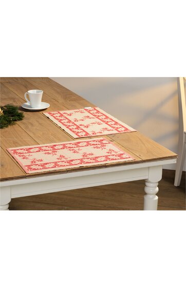 Rechteckige Tischsets in Cremeweiß mit rotem Blumenmuster, gesäumt, auf hellbraunem Holztisch mit weiß lackiertem Tischgestell, keine Personen sichtbar