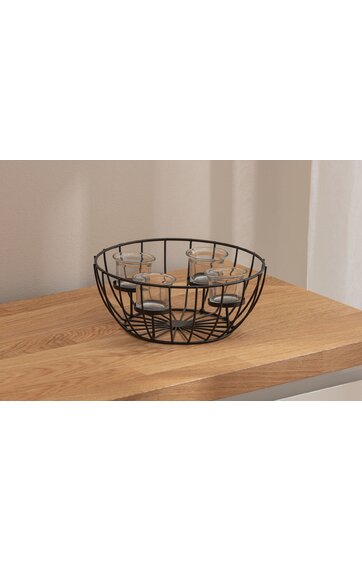 Schwarzer runder Metallkorb mit Gitterstruktur, enthält fünf durchsichtige Teelichthalter aus Glas, auf hellem Holztisch platziert