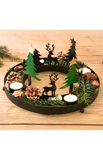 Runder Adventskranz in mattschwarz mit grünen Tannenbäumen, schwarzen Rentier-Silhouetten in der Mitte, vier weißen Teelichtern, braunen Tannenzapfen, kleinen goldfarbenen Kugeln und frischem grünen Tannengrün, auf hellbraunem Holztisch