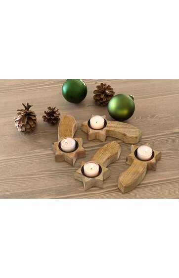 Vier kerzenhalter in sternform aus hellbraunem holz, jeweils mit weißer teelichtkerze, drei grüne kugeln und drei zapfen liegen auf hellbraunem holztisch