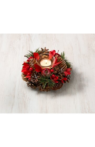 Runder Adventskranz mit braunen Tannenzapfen, grünen Kiefernzweigen, roten Beeren, mittig Glaswindlicht mit brennender Kerze, dekoration auf hellem Holztisch
