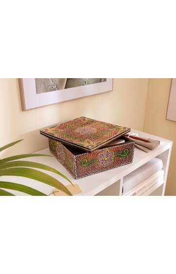 Quadratische Schmuckdose mit buntem Punktmuster in Rot, Grün, Gelb und Weiß, abnehmbare Deckel, liegend auf weißem Regal neben gefalteten Tüchern