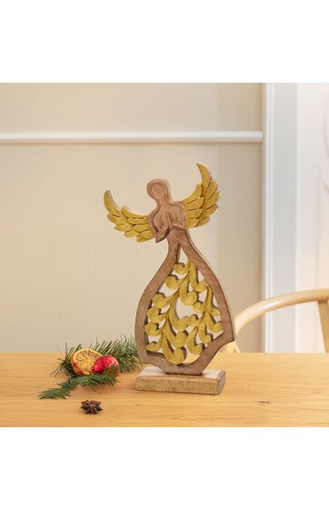 Dekofigur Engel aus Holz, naturbraun mit goldfarbenen Flügeln und goldfarbenen dekorativen Elementen im Kleid, stehende Form auf rechteckigem Sockel, auf hölzernem Tisch mit Tannenzweig und Weihnachtsdekoration