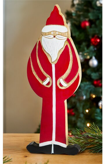 Dekofigur Weihnachtsmann in Rot mit weißem Bart, goldfarbenen Brillen und goldfarbenen Details, lange Mantelform, schwarze Schuhe, stehend auf Holzuntergrund vor Weihnachtsbaum