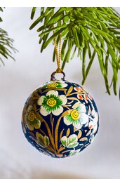 Weihnachtlicher Kugelanhänger, dunkelblau, mit buntem Blumenmuster in Gelb, Grün, Weiß und Orange, goldfarbener Aufhängebügel und Band, rund, glänzend, hängend an Tannenzweig