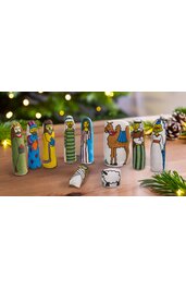 Neun bunte Spielfiguren aus Holz, bemalt als Weihnachtskrippenfiguren mit Meerjungfrau, König, Heiligen, Kamel, Schaf, liegende Figur, auf Holztisch vor unscharfem Lichterhintergrund