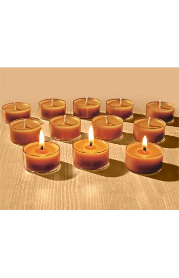 Zwölf runde Teelichtkerzen in transparenter Hülle, bernsteinfarben, drei Kerzen brennen, zehn Kerzen unbeleuchtet, angeordnet auf hellbrauner Holzoberfläche