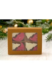 Braune Geschenkbox mit durchsichtigem Fenster, innen vier runde Schokoladen mit Weihnachtsbaum- und Halbmondmotiv, Schokoladen in Weiß und Dunkelrot, Box liegt auf hellen Holzdielen, Tannenzweige und Weihnachtskugeln im Hintergrund