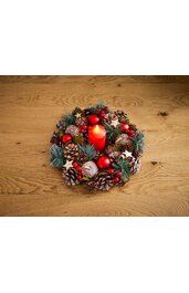 Adventskranz aus Tannenzweigen, roten Beeren und Zapfen, mit roten Kugeln und kleinen Sternen, rotes zylindrisches Bratapfelkerze in der Mitte, auf hellem Holzuntergrund