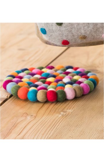 Bunter runder Untersetzer aus kleinen Filzkugeln in verschiedenen Farben, flach liegend auf hellem Holzbrett