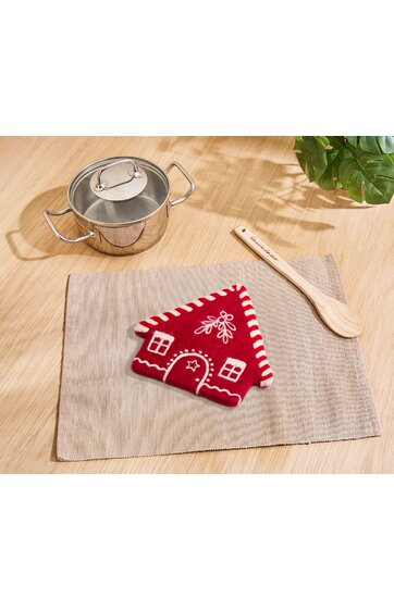 Kleine Aufbewahrungstasche in Form eines roten Lebkuchenhauses mit weißen Ziernähten und Fenstermotiven, dreieckige Dachform, liegt auf hellgrauer Stoffunterlage, daneben Holzlöffel und Edelstahl-Topf mit Glasdeckel auf Holzoberfläche