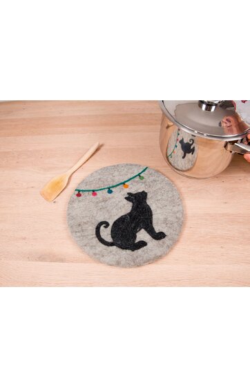 Runder grauer Topfuntersetzer mit schwarzer Katzen-Silhouette, bunter Lichterkette, auf hellem Holzuntergrund, daneben Holzlöffel und silberner Kochtopf mit Glasdeckel