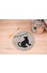 Runder grauer Topfuntersetzer mit schwarzer Katzen-Silhouette, bunter Lichterkette, auf hellem Holzuntergrund, daneben Holzlöffel und silberner Kochtopf mit Glasdeckel