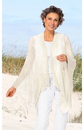 Ärmellose weiße Strickweste mit offenem Schnitt, lange Zipfel am Saum, getragen von lächelnder stehender Frau mit kurzem lockigem Haar, kombiniert mit weißem Langarmshirt und weißen Hosen, Strandhintergrund