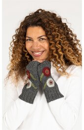 Gestrickte Handschuhe in Dunkelgrau mit bunten, runden Blumenmustern in Rot, Weiß und Beige, am Handgelenk anliegend, getragen von lächelnder Frau mit lockigem braunem Haar, weiße langärmlige Oberbekleidung