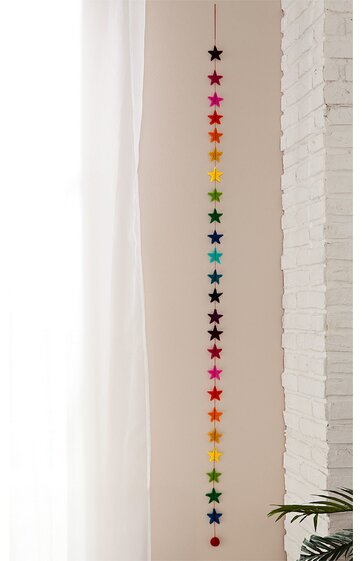 Lange Dekohänger mit Sternen, mehrfarbig in Regenbogenfarben, Sternform, hängend an weißer Wand neben weißem Vorhang, dekoratives Wandobjekt