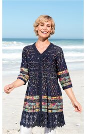 Dunkelblauer langer Pullover mit buntem Ethno-Muster, V-Ausschnitt, 3/4-Ärmel, gewellter Saum, getragen von lächelnder Frau am Strand, lockere Passform