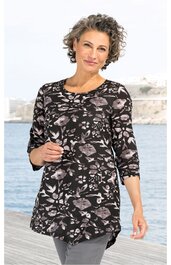 Schwarzes Longshirt mit floralen rosa und grauen Blumenmustern, Rundhalsausschnitt, 3/4-lange Ärmel, taillierte Form, getragen von stehender Frau mit verschränkten Armen am Wasserufer