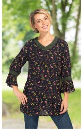 Dunkelblaue Tunika mit buntem Blumenmuster, V-Ausschnitt mit dunkelgrünem Rand, dreiviertellange Ärmel mit Volant und dunkelgrünen Bündchen, locker sitzend, getragen von lächelnder Frau draußen stehend
